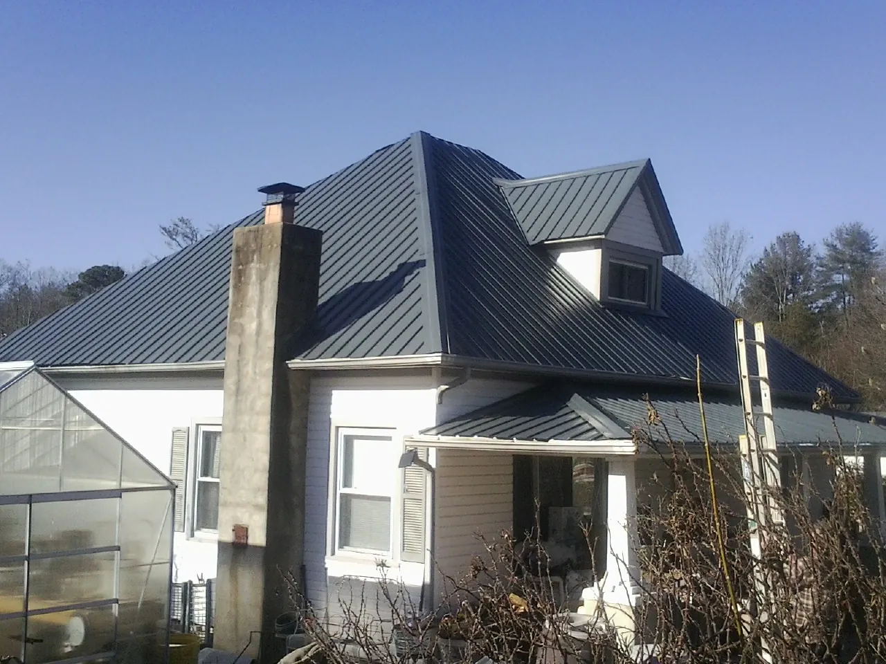 Dark blue standing seam metal roof on a white farmhouse with dormer — Slate & Tile Roof Repair by Roofing Brothers in Justin