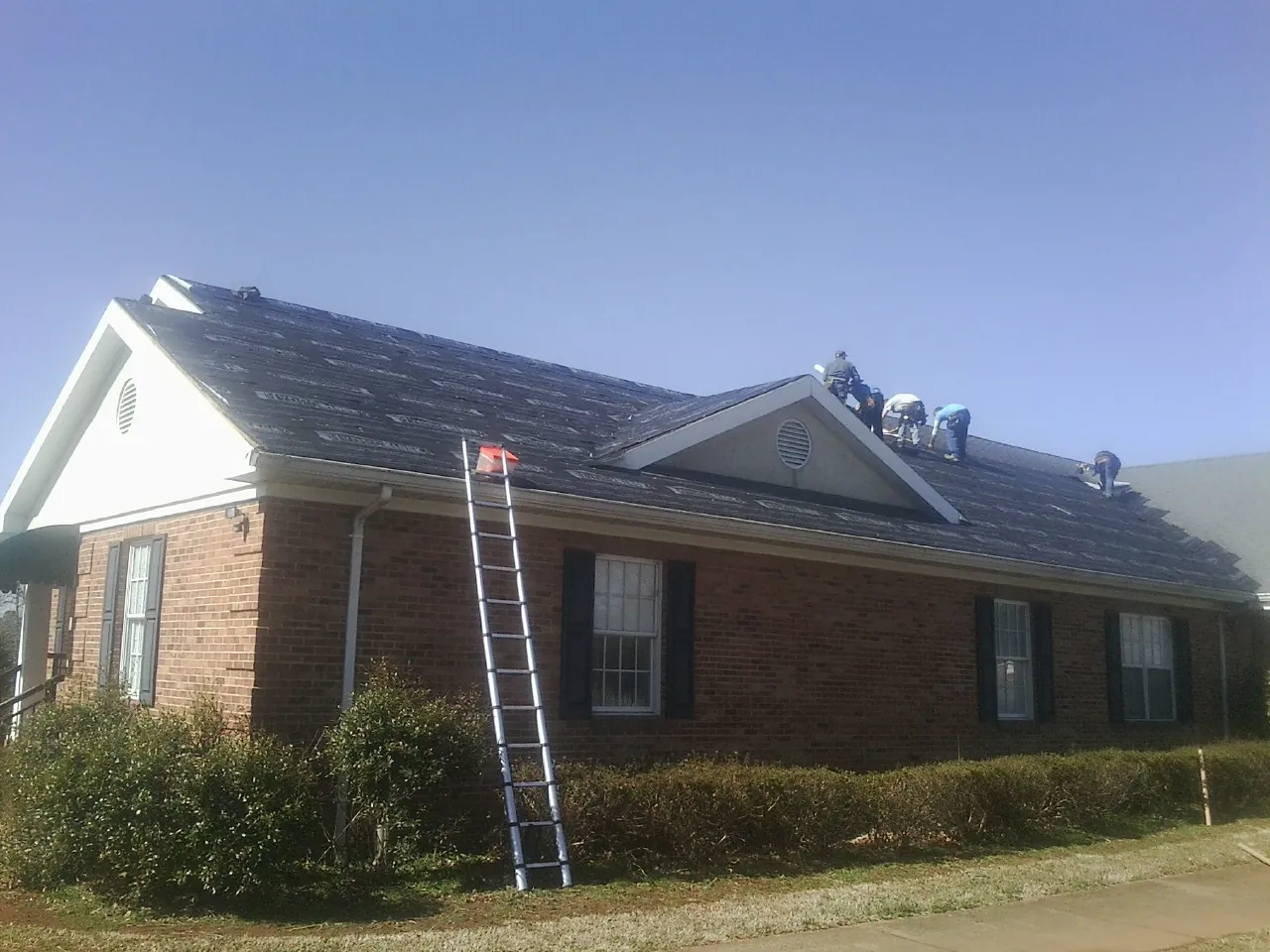 Crew tearing shingles off a brick ranch roof with a ladder set — Emergency Roof Repair work by our crew in Justin