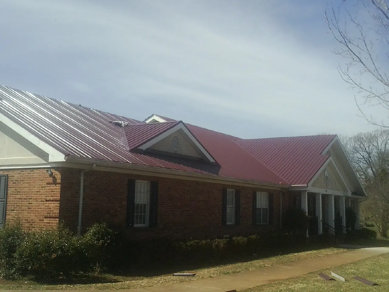Red metal roof with gabled entries on a long brick building, from a Hail Damage Roof Repair job in Justin