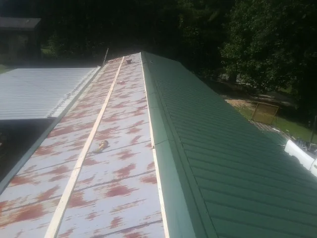 Old rusted panels beside newly installed green metal roofing — Wind Damage Roof Repair by Roofing Brothers in Justin