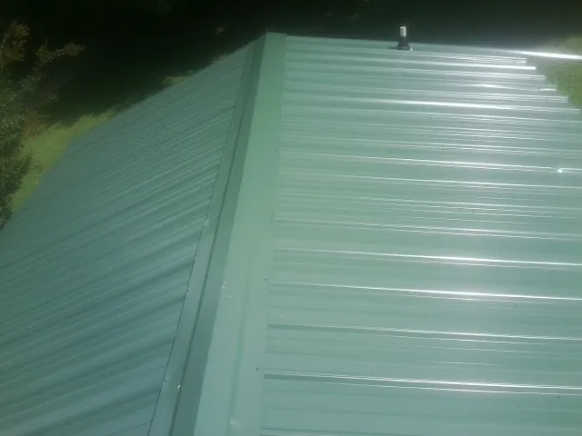 New green metal panels meeting at the ridge of a roof — Flat Roof Repair work by our crew in Justin