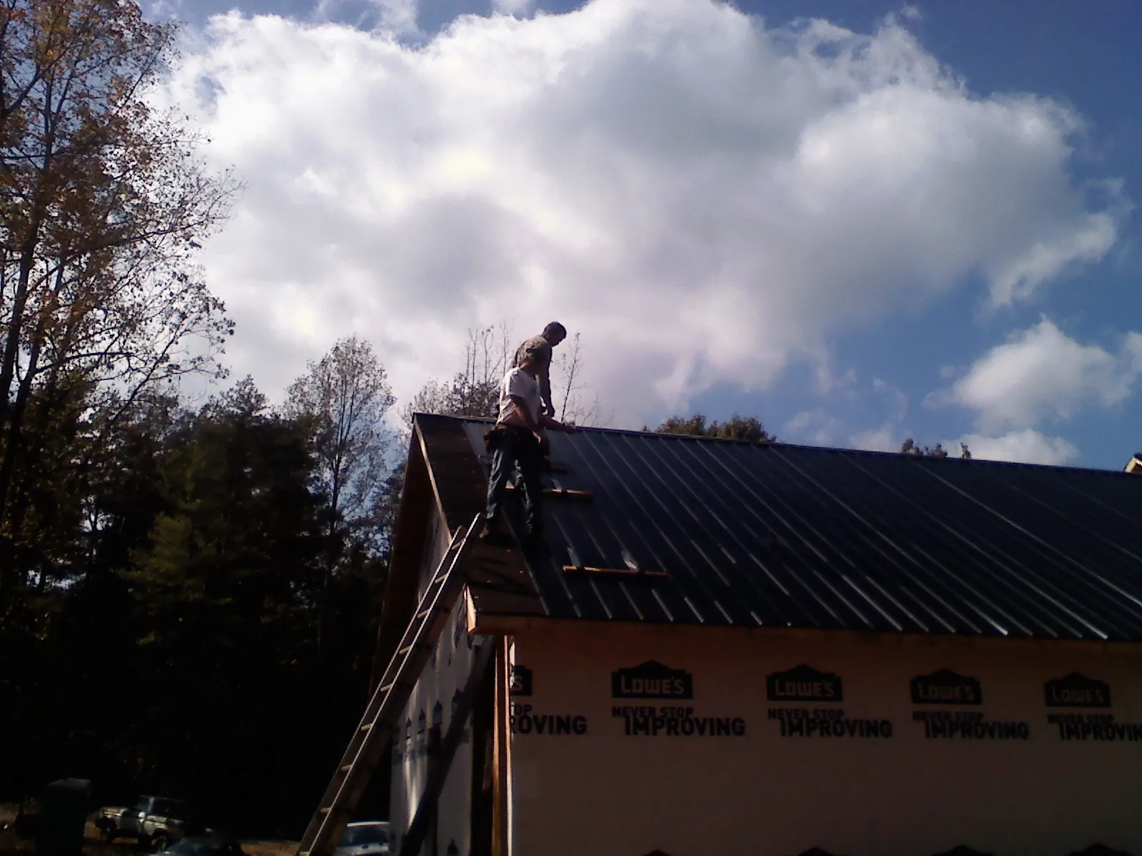 Roofer fastening dark metal panels high against a cloudy sky, from a Roof Inspection job in Justin